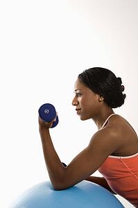 Profile of African American young adult woman leaning on exercise ball holding dumbbell.
