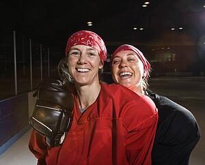 Women hockey players in uniform posing with helmets off on ice rink