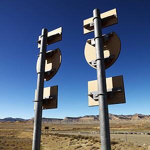 Two road signs on a psot with guardrail and mountains in background.