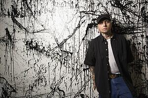 Tattooed and pierced man standing against paint splattered background