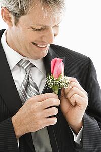 Caucasian groom adjusting boutonniere.