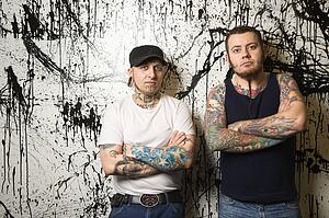 Tattooed men standing against paint splattered background