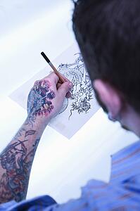 Caucasian male tattoo artist drawing tattoo on light table.