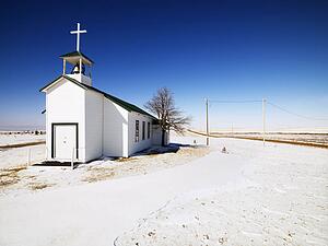 White small church with snow covered ground in foreground.