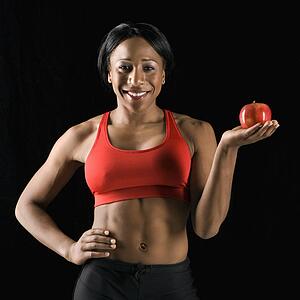 Smiling African American young adult woman holding apple with hand on hip.