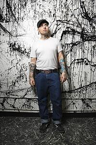 Tattooed and pierced man standing against paint splattered background