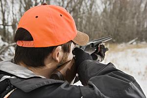 Male aiming shotgun towards woods