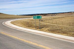 Winding road in South Dakota with mileage distance road sign.