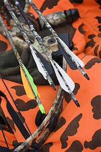 Still life shot of bow and arrows laying against blaze orange camouflage.