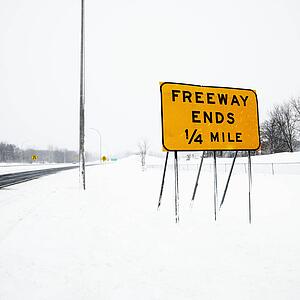 Snow covered highway with sign reading Freeway ends quarter mile.