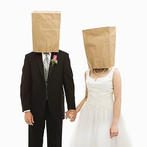Caucasian groom and Asian bride with brown paper bags over their heads.