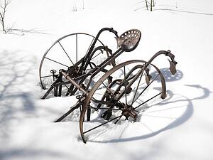 Classic metal plow sitting in snow covered field.