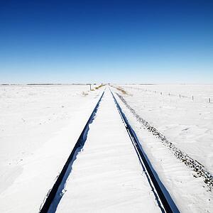Snow covered railroad tracks leading to a blue sky 