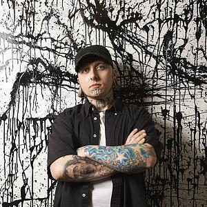 Tattooed and pierced man standing against paint splattered background.