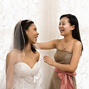 Asian bridesmaid laughing with African-American bride.