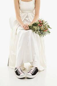 Caucasian bride holding bouquet exposing her tennis shoes.