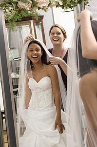 Seamstress helping bride with veil in bridal shop
