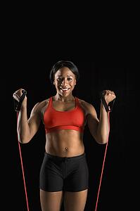 African American young adult woman exercising with resistance tube and smiling at viewer.