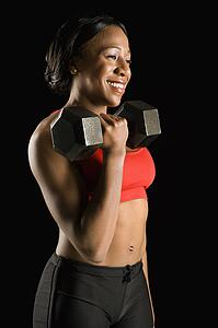 Smiling African American young adult woman holding dumbbell.