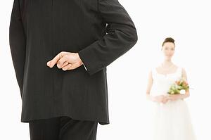 Back of groom with his fingers crossed and bride in background