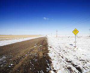 Desolate dirt road with snow covered ground and road sign.