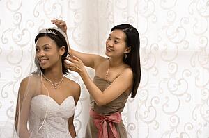 Bridesmaid adjusting veil of a bride.