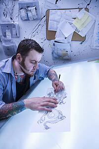Caucasian male tattoo artist drawing tattoo on light table.