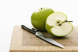 Still life of green apples and knife on cutting board.
