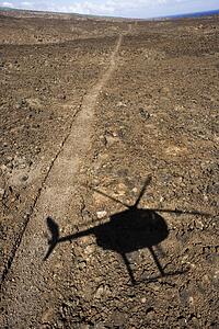Pathway leading through rocky terrain with shadow of helicopter flying overhead in Maui, Hawaii.