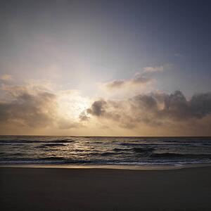 Beach with sun setting in clouds over ocean at Bald Head Island, North Carolina