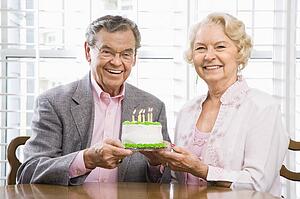 Couple holding birthday cake looking at viewer.