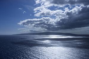 Island in Pacific ocean with puffy clouds.
