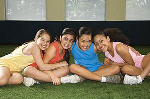 Four multiethnic girls sitting with arms around eachother smiling.