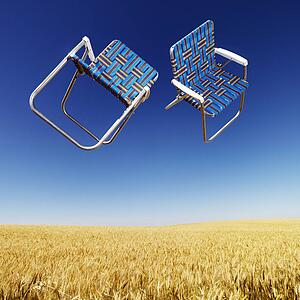 Two lawn chairs in mid-air above a field of wheat with blue sky.