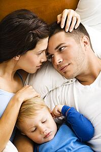 Parents cuddling with toddler son in bed.