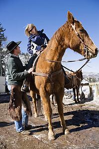 Wrangler talking to young woman on horseback.