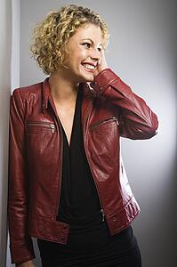 Young adult woman wearing red jacket smiling with hand to face.
