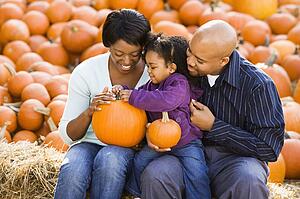 Happy smiling family sitting on hay bales and holding pumpkins at outdoor market