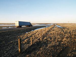 Transfer truck driving through rural setting.
