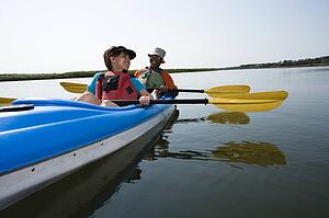 African American middle-aged couple sitting in kayak on lake smiling and laughing.