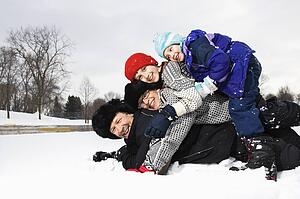 Happy family of four laying stacked on top of each other in snow smiling 