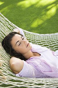 Pretty young adult brunette woman laying in hammock with arms behind head sleeping