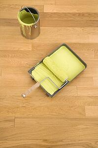 Still life of paint roller in tray with paint can on wood floor.