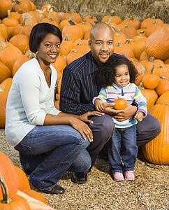 Parents and daughter picking out pumpkin at outdoor market