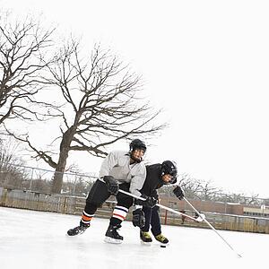 Two boys in ice hockey uniforms playing hockey on ice rink