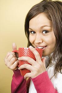 Woman holding coffee cup to lips and smiling at viewer