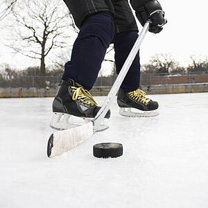 Boy in ice hockey uniform skating on ice rink moving puck