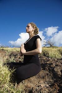 Side view of a woman sitting in yoga lotus position on rocks in Maui, Hawaii