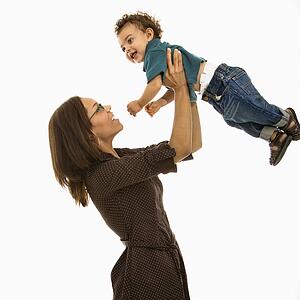 Side view of mid adult African American mom lifting happy toddler son into air above head.