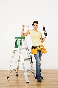 Woman standing in home with ladder and holding tools smiling
